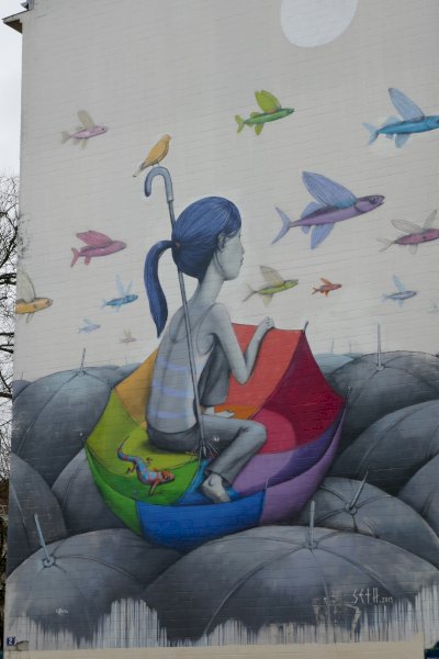 Street art of a girl sitting inside a brightly coloured umberella as fish fly over head