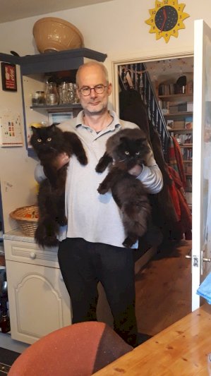Professor Straub is wearing a casual top and holding a big, fluffy black cat under each arm