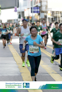 Dr Chan is running in an organised event. She is wearing a light blue tshirt and has a race number - G2705 - pinned to her front. The banner at the bottom of the image says "Standard Chartered Hong Kong Marathon 2021"