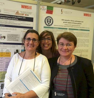Dr Bonne stands with two colleagues in front of a WMS poster display